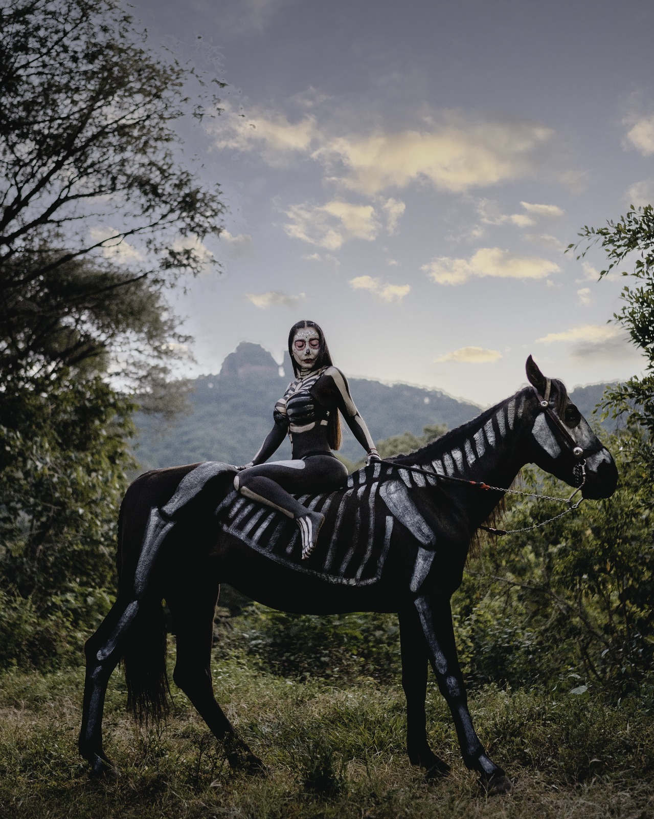 Catrina caracterizada como jinete junto a caballo negro maquillado para sesión fotográfica de Día de Muertos
